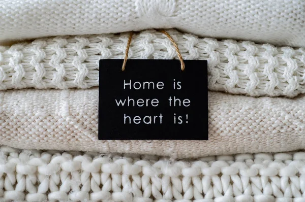Inscription HOME IS WHERE THE HEART IS Background with warm sweaters. Pile of knitted clothes in warm shades, space for text, Autumn winter concept. Copy Space. — Stock Photo, Image