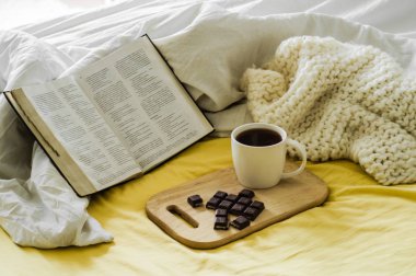 Güneş tarafından aydınlatılmış İncil ile sabah kahve. Christian Bible ile kahve fincan. Beyaz yatak odası. Çikolata ve kahve Kupası.