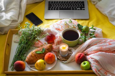 Yatakta, bir tepsi çay, kruvasan, meyve, çiçek ve dizüstü sabah kahvaltı. Blogger tema. evde çalışma kavramı