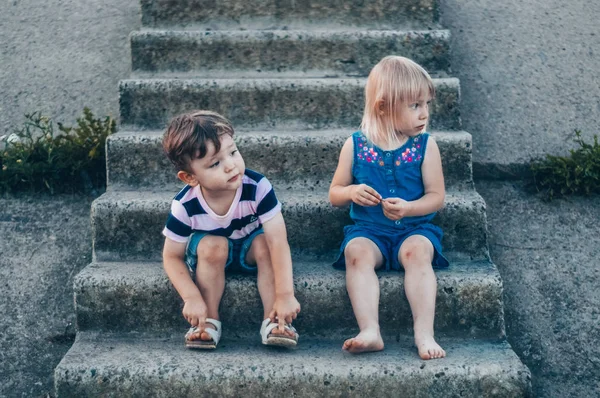 Dua anak kecil, gadis dan anak laki-laki di alam, duduk di tangga batu tampak samping, luar ruangan. Ruang untuk Teks. Bernada retro. Musim gugur musim panas — Stok Foto