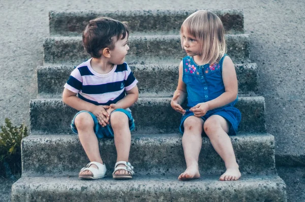 Дві маленькі дитини, дівчинка і хлопчик в природі, сидять на камені, дивлячись один на одного з посмішкою, на відкритому повітрі. Ретро тоноване. Літо — стокове фото
