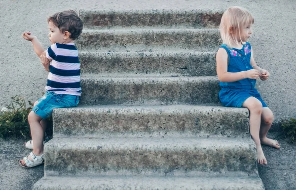 Dua anak kecil, gadis dan anak laki-laki di alam, duduk di tangga batu tampak samping, luar ruangan. Ruang untuk Teks. Bernada retro. Musim gugur musim panas — Stok Foto