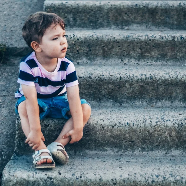 Anak kecil yang duduk di tangga batu melihat ke bawah, melihat termenung dan memegang tangannya di luar ruangan. Ruang untuk Teks. Bernada retro. Musim panas — Stok Foto
