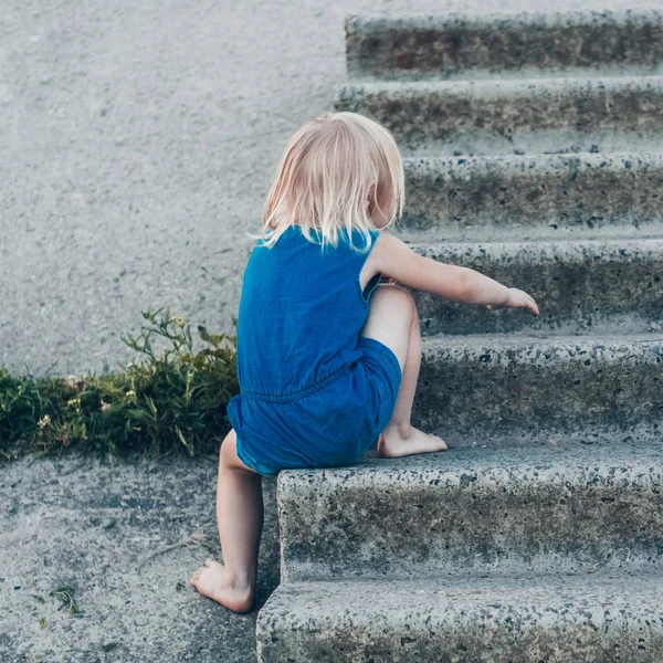 Gadis kecil yang lucu tertawa di alam - gadis bahagia dengan gaun biru dan dipukuli dengan lutut duduk di tangga. Happy childhood — Stok Foto