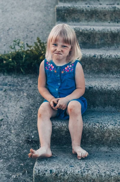 Schattig meisje lachen over aard - gelukkig meisje in een blauwe jurk en geslagen door de knieën zit op de trap. Gelukkige jeugd — Stockfoto