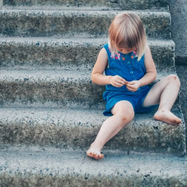 Schattig meisje lachen over aard - gelukkig meisje in een blauwe jurk en geslagen door de knieën zit op de trap. Gelukkige jeugd — Stockfoto