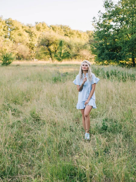 Retrato de una hermosa chica en un vestido azul con un dolor de cabeza en un campo al atardecer en verano. Ropa de verano casual. Primer plano — Foto de Stock