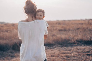Genç Anne küçük oğlu, kisses günbatımında çayırda güneşli. Oğlu tutan anne. Anneler günü. Aile kavramı