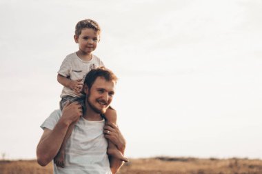 Mutlu çocuk babamla oynuyor. Babam ve oğlum dışarıda. Babası çocuğu sırtında taşıyor. Yaz tarlasında mutlu aile