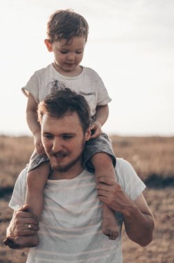 Mutlu çocuk babamla oynuyor. Babam ve oğlum dışarıda. Babası çocuğu sırtında taşıyor. Yaz tarlasında mutlu aile