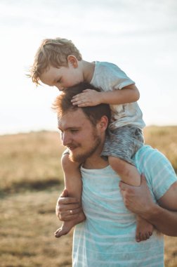 Mutlu çocuk babamla oynuyor. Babam ve oğlum dışarıda. Babası çocuğu sırtında taşıyor. Yaz tarlasında mutlu aile