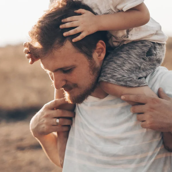 Um miúdo feliz a brincar com o pai. Pai e filho ao ar livre. Pai carregando criança em suas costas. Família feliz no campo de verão — Fotografia de Stock