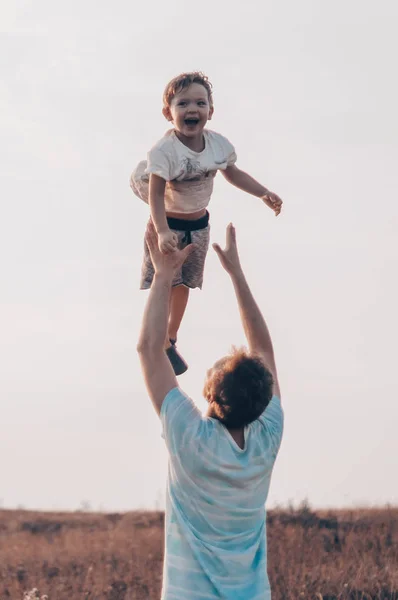 Padre lanza a su lindo y pequeño hijo al aire libre. Día del Padre, Padre y su hijo bebé jugando y abrazándose al aire libre . — Foto de Stock