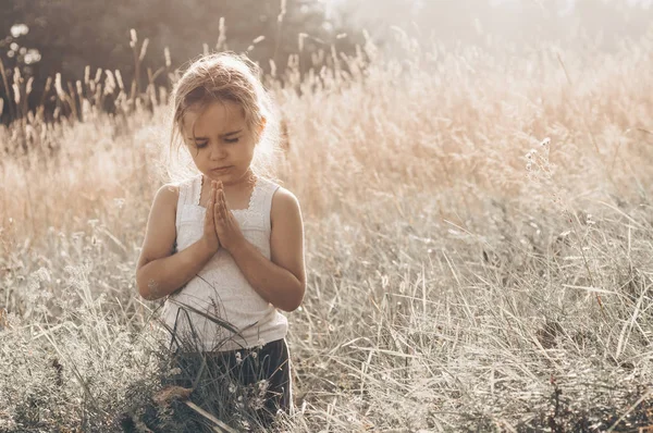 Gadis kecil menutup matanya berdoa saat matahari terbenam. Tangan dilipat dalam konsep doa untuk iman, spiritualitas dan agama. Harapan, konsep . — Stok Foto