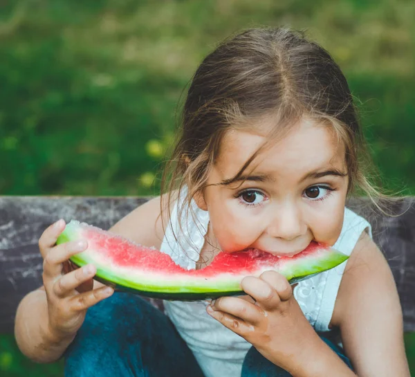 Niño comiendo sandía en el jardín. Los niños comen fruta al aire libre. Snack saludable para niños. Fondo hermoso, chica de la emoción — Foto de Stock