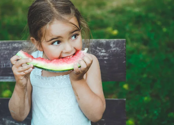 Niño comiendo sandía en el jardín. Los niños comen fruta al aire libre. Snack saludable para niños. Fondo hermoso, chica de la emoción — Foto de Stock