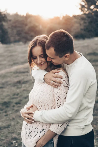 Vientre de una mujer embarazada. Pareja con una mujer embarazada cogida de la mano al atardecer en un ambiente romántico en verano . — Foto de Stock