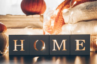 Background with warm sweaters and the inscription HOME. Pile of knitted clothes with leaves, pumpkins. Coziness. Autumn concept