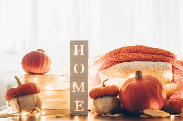 Background with warm sweaters and the inscription HOME. Pile of knitted clothes with leaves, pumpkins. Coziness. Autumn concept