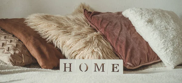 Still life details in home interior of living room and the inscription HOME. A lot of decorative cozy pillows. HOME concept