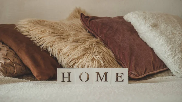 Still life details in home interior of living room and the inscription HOME. A lot of decorative cozy pillows. HOME concept