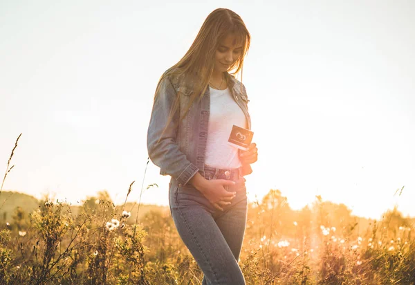 Young Pregnant Woman holding ultrasound photo at Sunset and Embracing her Belly. 4 Month Pregnancy. Maternity Concept. Toned Photo — Stock Photo, Image