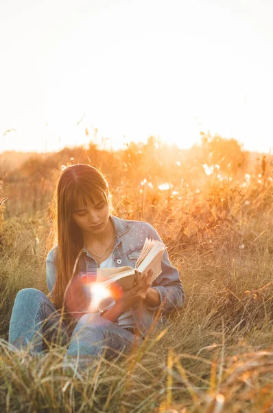 Belle fille en champ d'automne lisant un livre. La fille assise sur une herbe, lisant un livre. Repose-toi et lis. Lecture extérieure — Photo