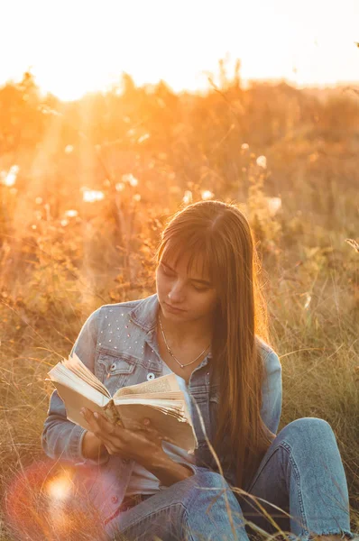 Mooi meisje in herfst veld lezen van een boek. Het meisje zittend op een gras, lezen van een boek. Rust en lezing. Buiten lezing — Stockfoto