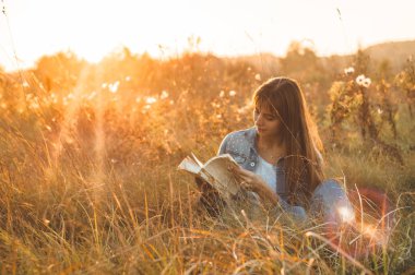 Güzel kız sonbahar alanında bir kitap okuma. Bir kitap okuma bir çim üzerinde oturan kız. Dinlenme ve okuma. Açık okuma
