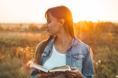 Güzel kız sonbahar alanında bir kitap okuma. Bir kitap okuma bir çim üzerinde oturan kız. Dinlenme ve okuma. Açık okuma