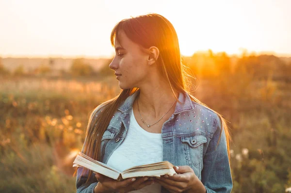 Mooi meisje in herfst veld lezen van een boek. Het meisje zittend op een gras, lezen van een boek. Rust en lezing. Buiten lezing — Stockfoto