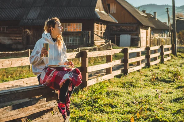 Girl sits on a wooden bench in the mountains in nature, reads a book, drinks hot tea from a thermo cup. Concepts Reading in nature — Stock Photo, Image