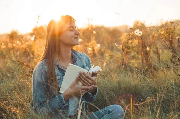 Mooi meisje in herfst veld lezen van een boek. Het meisje zittend op een gras, lezen van een boek. Rust en lezing. Buiten lezing — Stockfoto