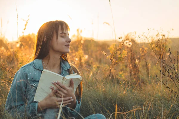 Mooi meisje in herfst veld lezen van een boek. Het meisje zittend op een gras, lezen van een boek. Rust en lezing. Buiten lezing — Stockfoto