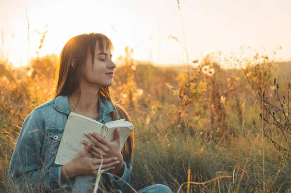 Gadis cantik di musim gugur membaca buku. Gadis yang duduk di rumput, membaca buku. Istirahat dan membaca. Pembacaan luar ruangan Stok Gambar Bebas Royalti