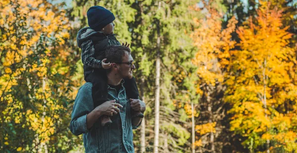 Father pointing out something to son in the autumn forest while holding him in arms