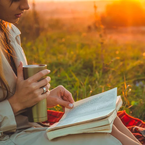 Het concept van levensstijl outdoor recreatie in het najaar. Meisje met hoed lezen boeken op plaid met een thermo-kop. Herfst. Zonsondergang. Gezellige — Stockfoto