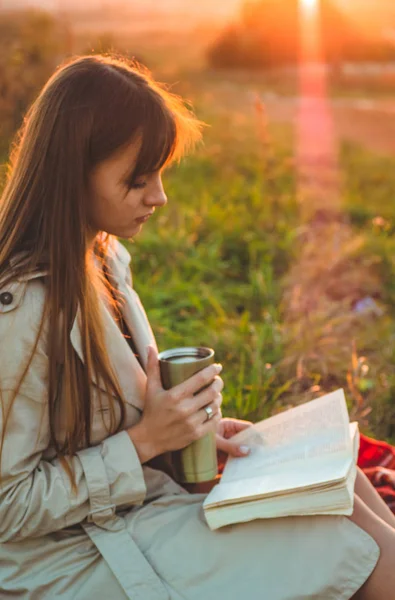 Het concept van levensstijl outdoor recreatie in het najaar. Meisje met hoed lezen boeken op plaid met een thermo-kop. Herfst. Zonsondergang. Gezellige — Stockfoto