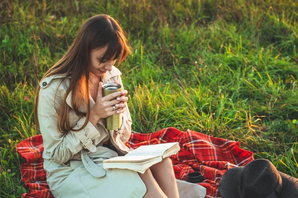 Het concept van levensstijl outdoor recreatie in het najaar. Meisje met hoed lezen boeken op plaid met een thermo-kop. Herfst. Zonsondergang. Gezellige — Stockfoto