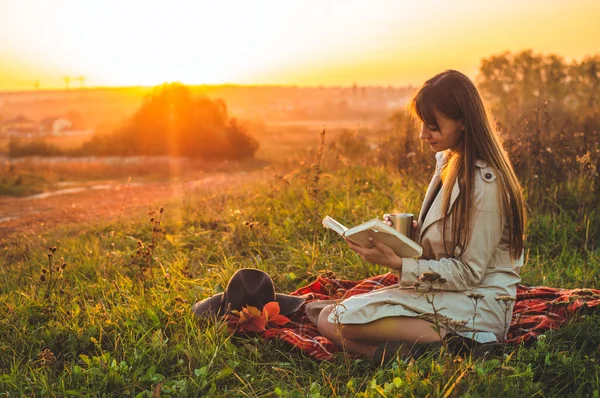 O conceito de estilo de vida recreação ao ar livre no outono. Menina com chapéu ler livros sobre xadrez com uma taça térmica. Outono. Pôr do sol. Aconchegante — Fotografia de Stock