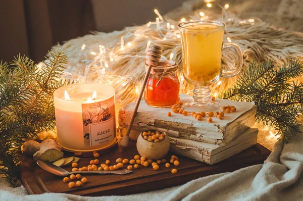Tea with sea-buckthorn berries and ginger on old books, honey, candle and conifer branches. The atmosphere of comfort at home — Stock Photo, Image