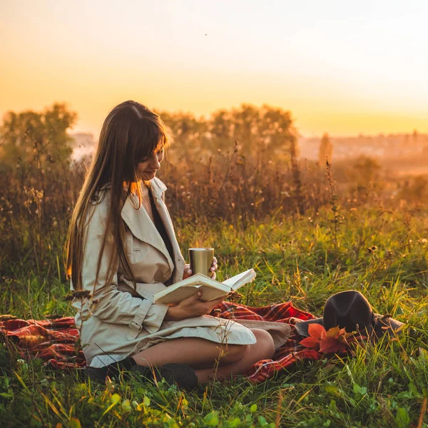 Le concept de loisirs de plein air style de vie en automne. Fille avec chapeau lire des livres sur plaid avec une tasse thermo. Automne. Coucher de soleil. Confortable — Photo