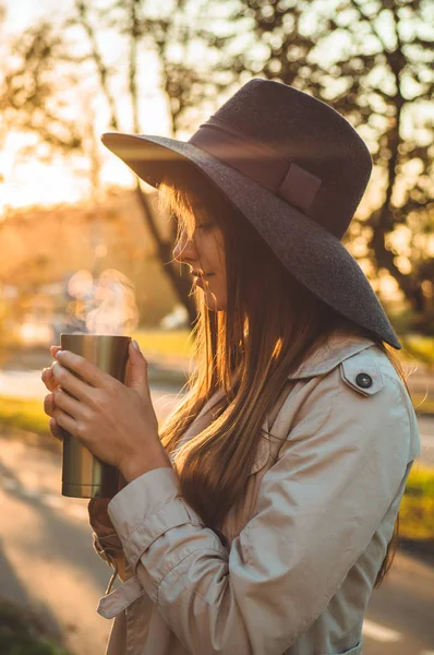 Mladá žena v klobouku s termosku termo pohár venkovní portrét v měkké slunečného letního. Na podzim. Západ slunce. Cozy — Stock fotografie