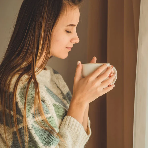 Útulný domov. Žena s šálkem horkého nápoje u okna. Při pohledu na okna a pití čaje. Dobré ráno s čajem. Mladá dívka relaxační — Stock fotografie