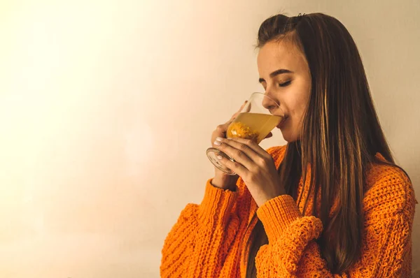 Прекрасная счастливая молодая женщина пьет чашку чая из облепихи. В кровати в ярко-оранжевом свитере. Портрет улыбающейся девушки крупным планом — стоковое фото