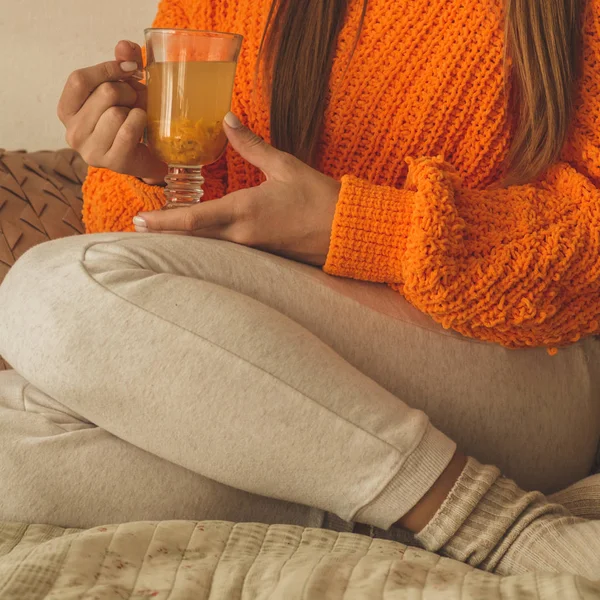 Hermosa mujer joven feliz beber taza de té de espino cerval de mar. En la cama en un suéter naranja brillante. Primer plano retrato de chica sonriente — Foto de Stock