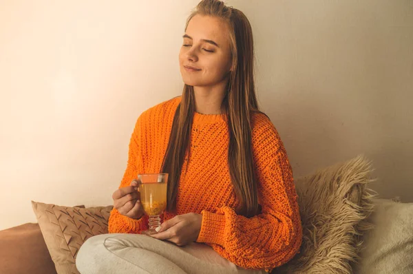 Hermosa mujer joven feliz bebiendo taza de café o té. En la cama en un suéter naranja brillante. Primer plano retrato de chica sonriente — Foto de Stock