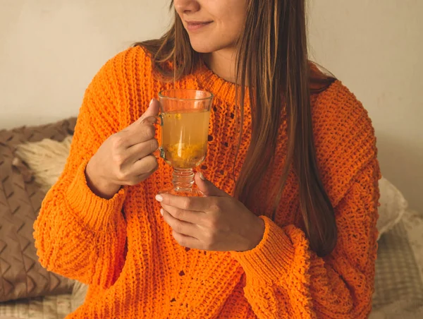 Hermosa mujer joven feliz bebiendo taza de café o té. En la cama en un suéter naranja brillante. Primer plano retrato de chica sonriente — Foto de Stock