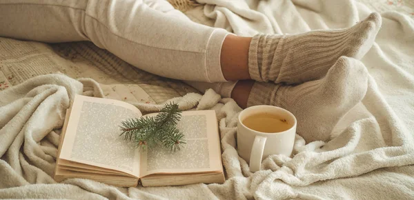 Noite de inverno aconchegante, meias de lã quentes. A mulher está deitada em cima de um cobertor branco desgrenhado e a ler livros. Cena de lazer acolhedor — Fotografia de Stock