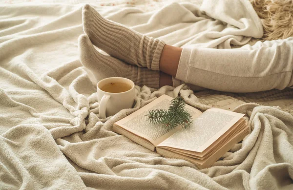 Noite de inverno aconchegante, meias de lã quentes. A mulher está deitada em cima de um cobertor branco desgrenhado e a ler livros. Cena de lazer acolhedor — Fotografia de Stock